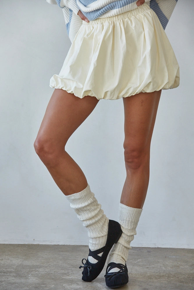Person wearing a white skirt, striped sweater, and knee-high socks with black shoes on a plain background