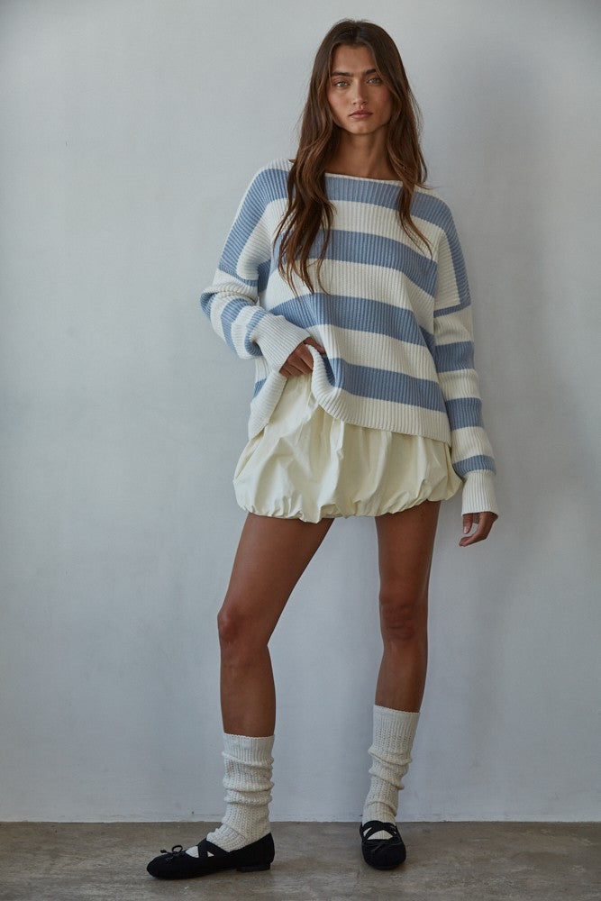 Woman wearing a blue and white striped sweater with a yellow skirt against a plain background