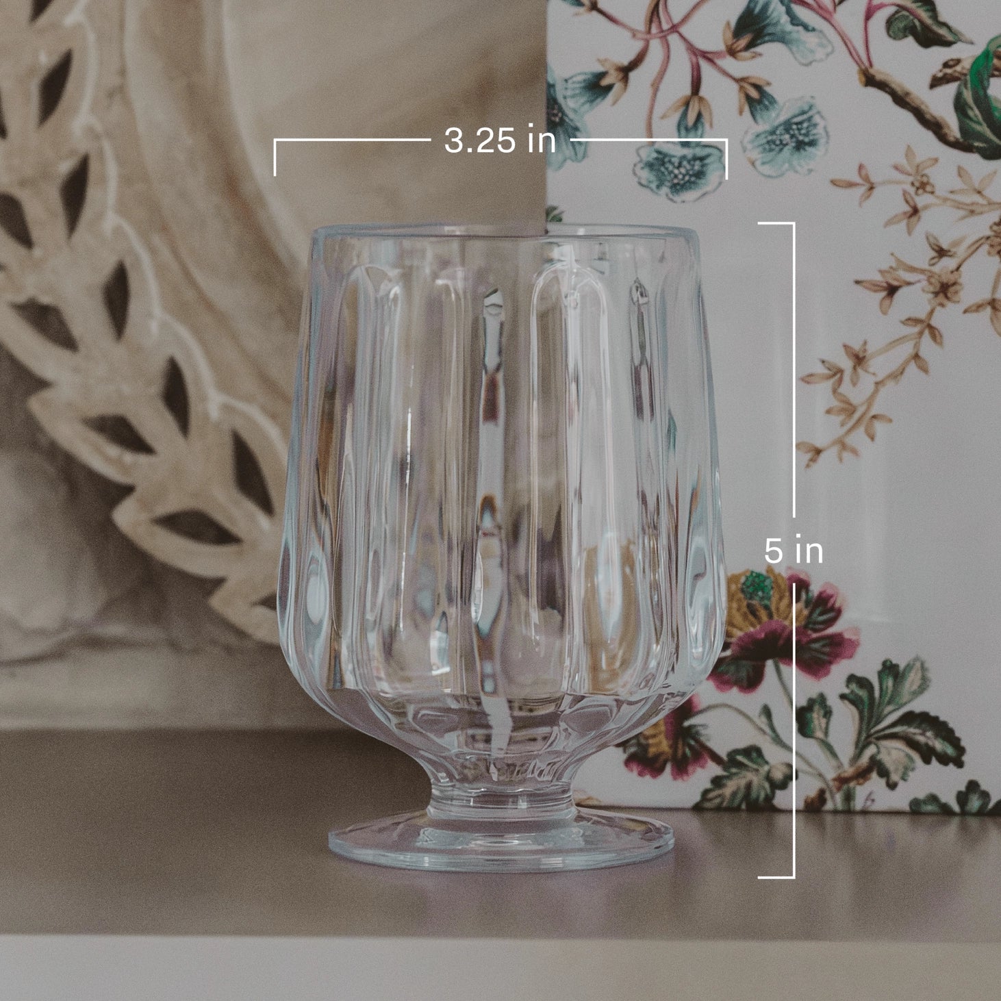 Clear glass with dimensions labeled, placed on a surface with decorative elements in the background.