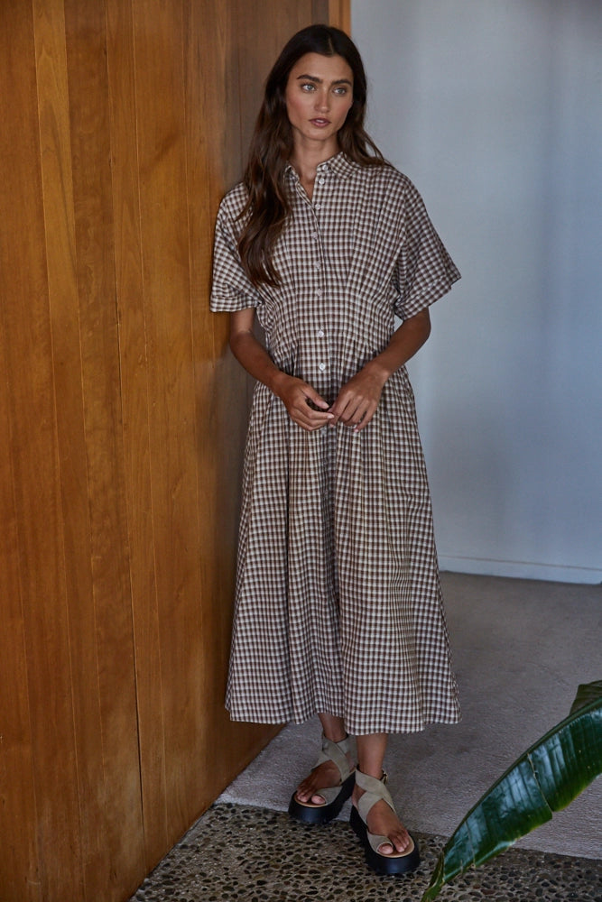 Woman wearing a checkered dress standing against a wooden wall.