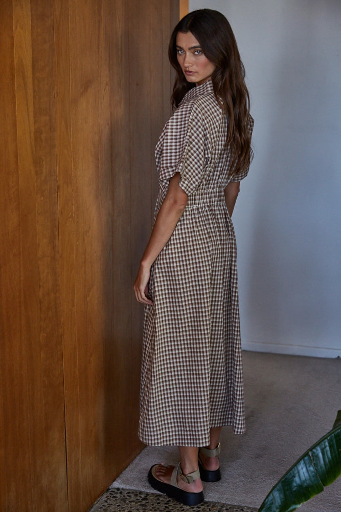 Woman wearing a checkered dress standing against a wooden wall.