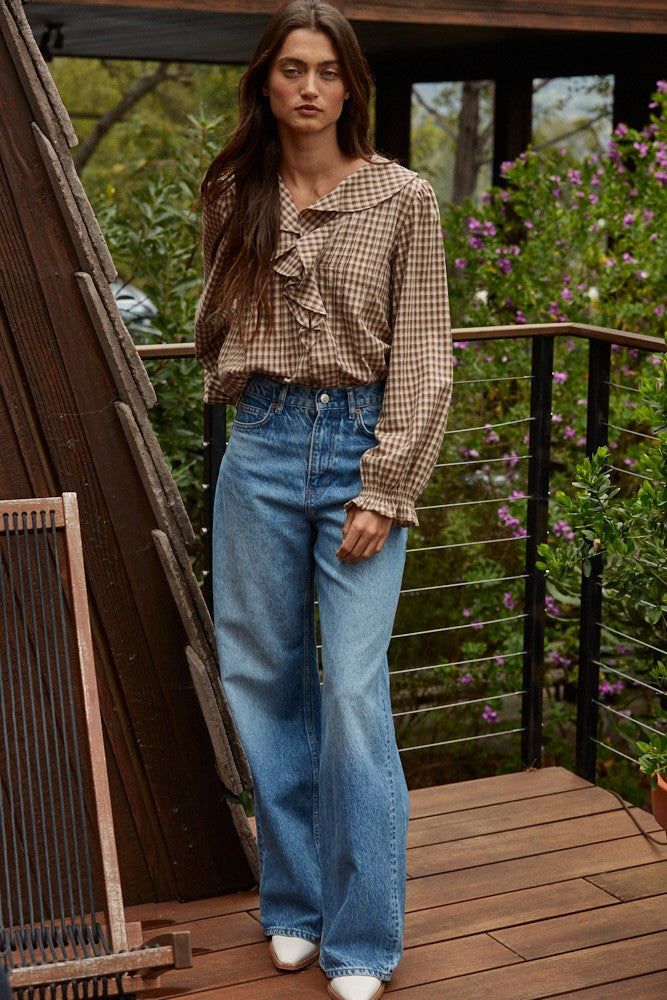Woman in plaid shirt and blue jeans standing on a wooden deck with greenery in the background