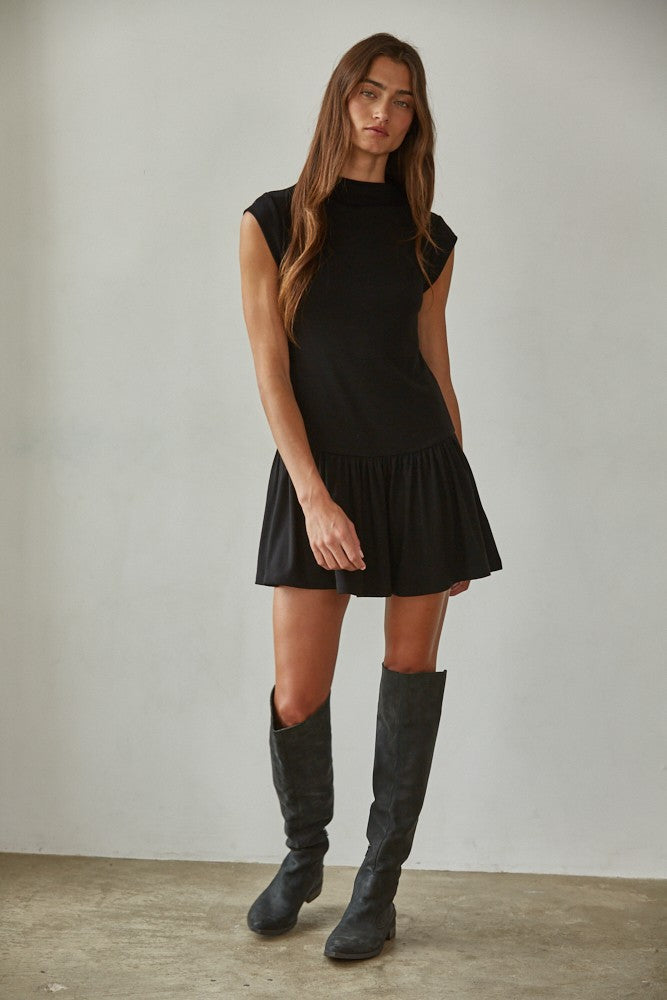 Woman wearing a black dress and knee-high boots against a plain background