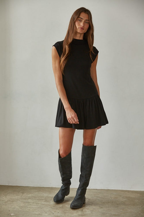 Woman wearing a black dress and knee-high boots against a plain background