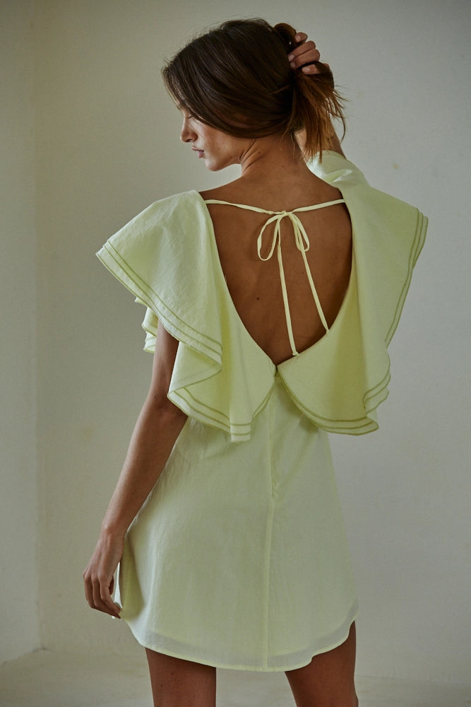 Woman wearing a light green dress with a backless design against a plain background