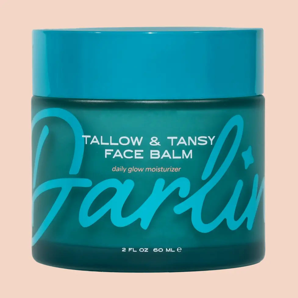Green jar of Tallow & Tansy Face Balm with blue lid on a beige background