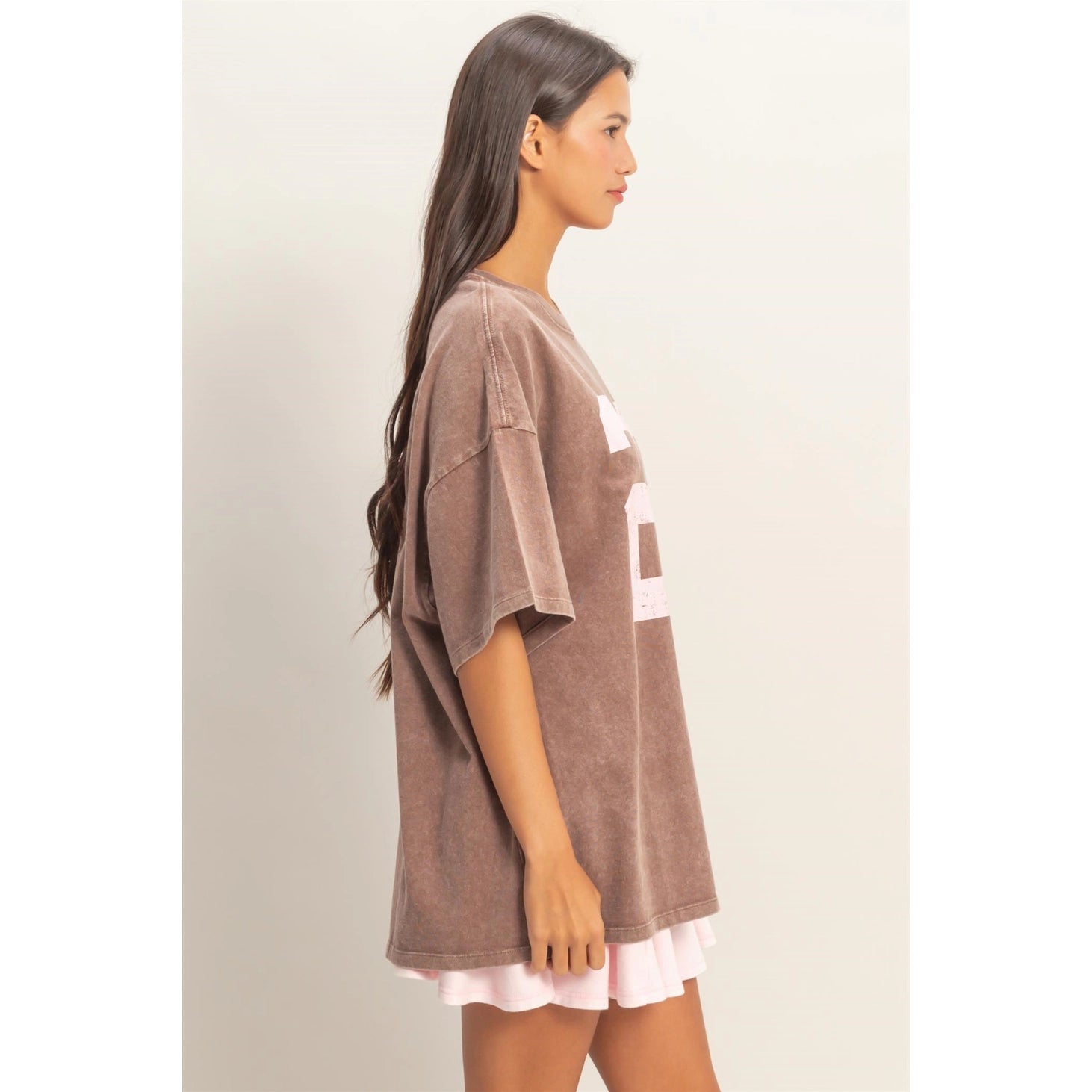 Woman wearing a brown oversized t-shirt with a white undershirt underneath on a plain background