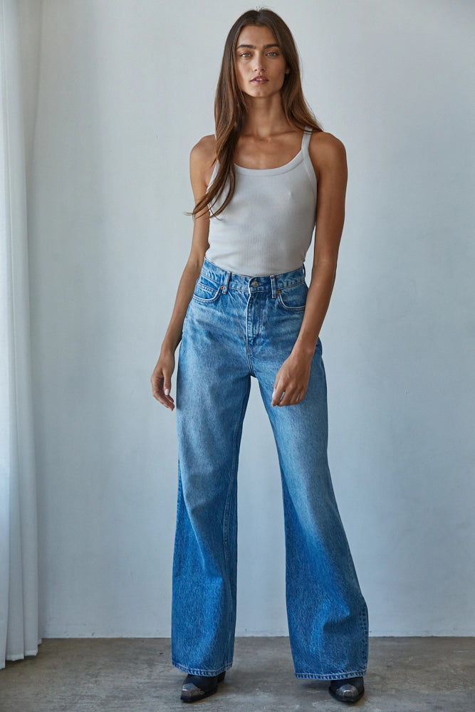 Woman wearing a white tank top and blue jeans against a plain background