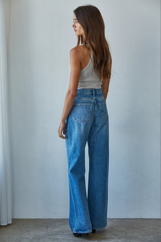 Woman wearing blue jeans and a white top against a plain background