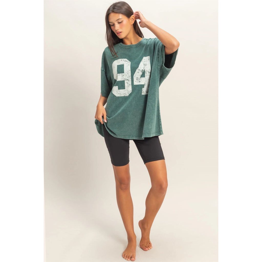 Woman wearing a green oversized t-shirt with the number 94 and black shorts on a white background